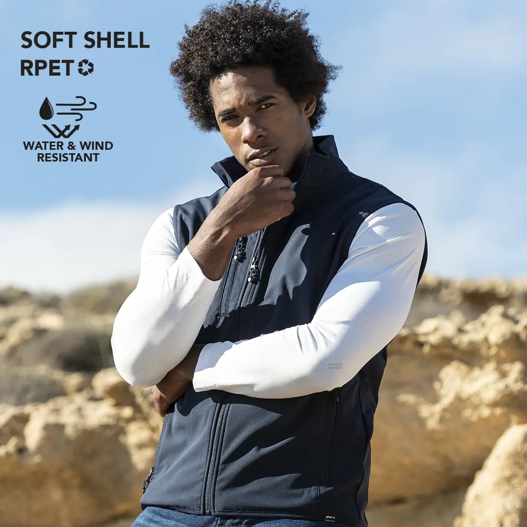 Hombre al aire libre con chaleco softshell resistente al agua y al viento junto a formaciones rocosas.
