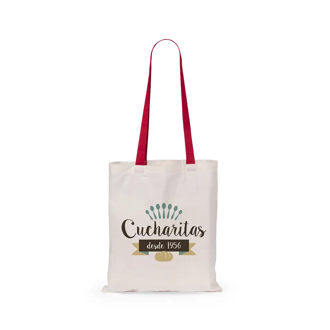 Bolsa de tela blanca con asas rojas estampada con el logo Cucharitas desde 1956 y cucharillas verdes sobre un pan.