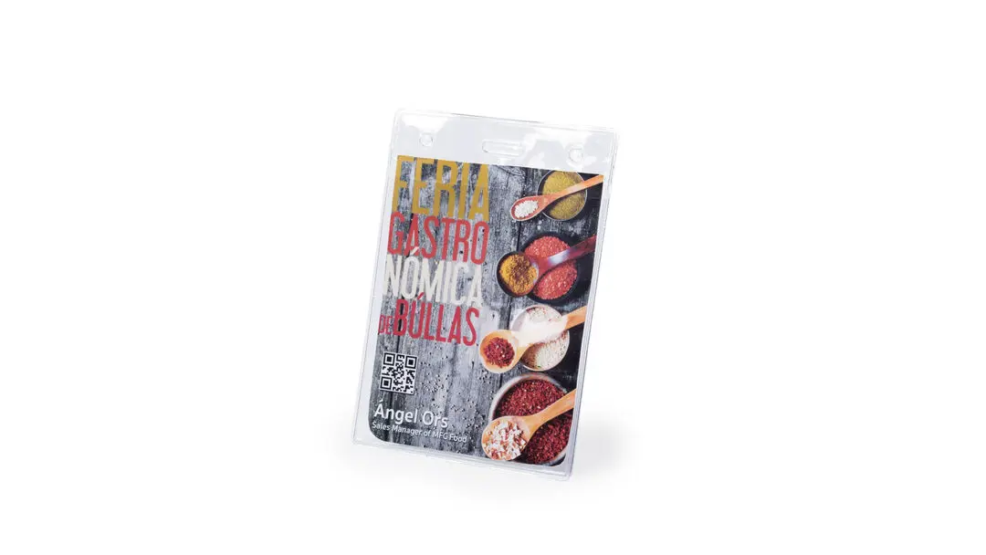 insignia de plástico con tarjeta de la Feria Gastronómica de Bullas y cucharas con especias coloreadas sobre fondo de madera