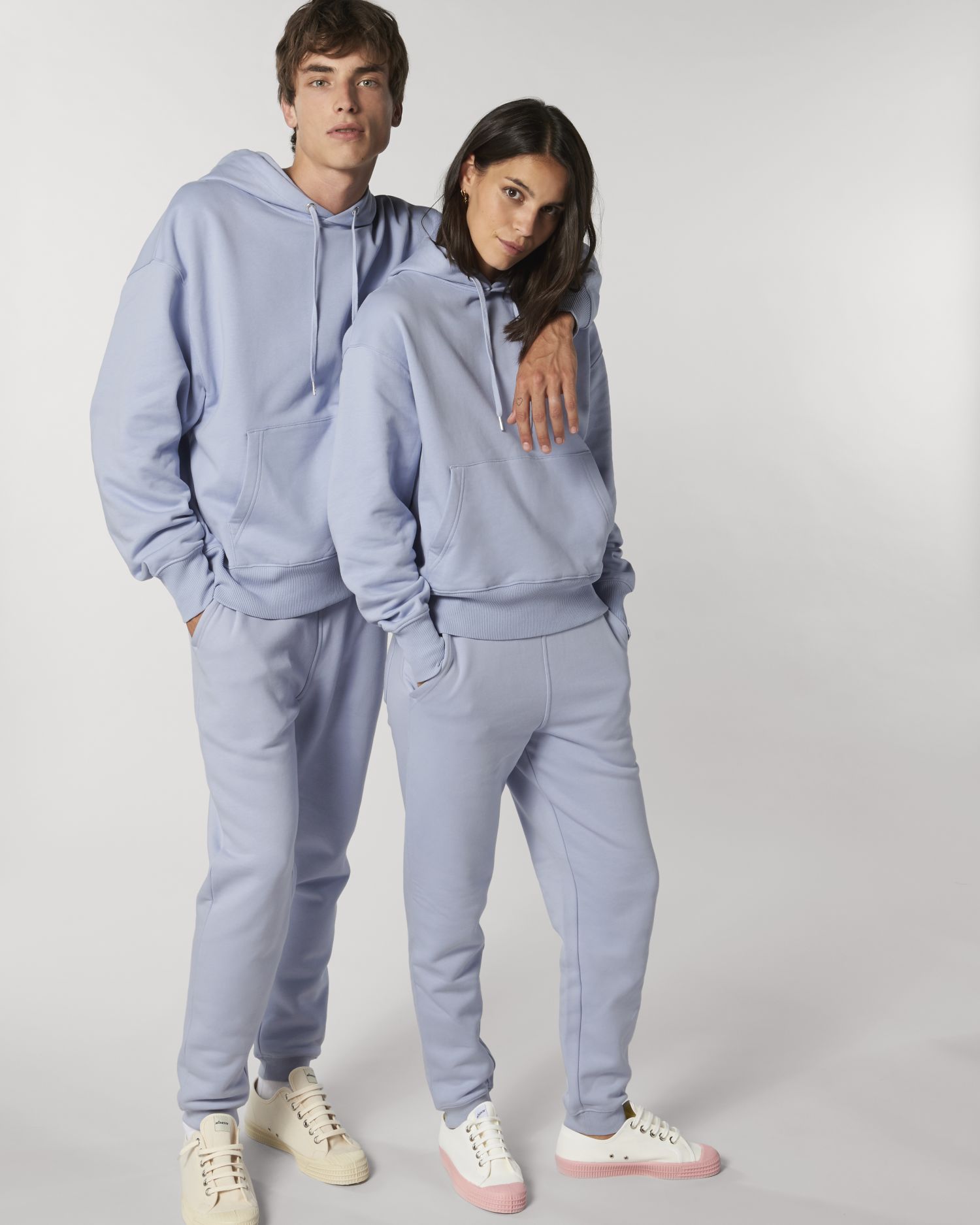 Pareja joven con sudaderas y pantalones deportivos azul claro posando sobre fondo blanco