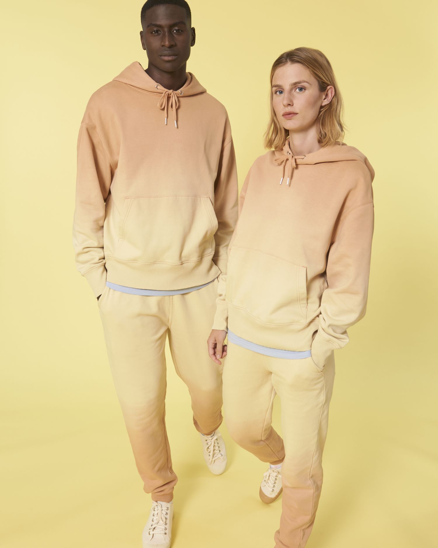 Hombre y mujer con sudadera y pantalón degradado en tonos pastel sobre fondo amarillo