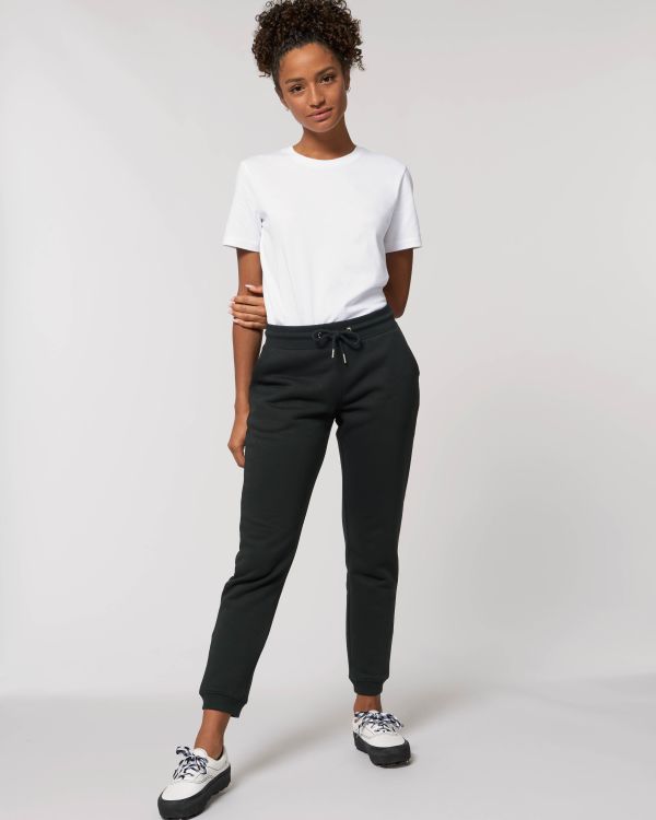 Mujer joven con camiseta blanca, pantalones jogger negros y zapatillas casuales sobre fondo neutro.