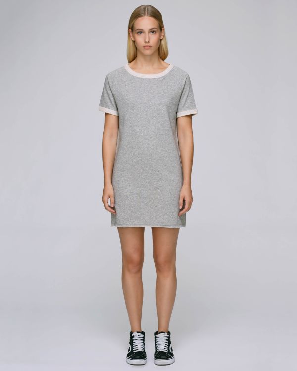 Mujer joven de pie con vestido gris corto de algodón y zapatillas negras sobre fondo neutro