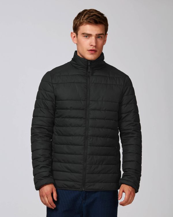 Hombre joven con chaqueta acolchada negra de cremallera en fondo neutro.