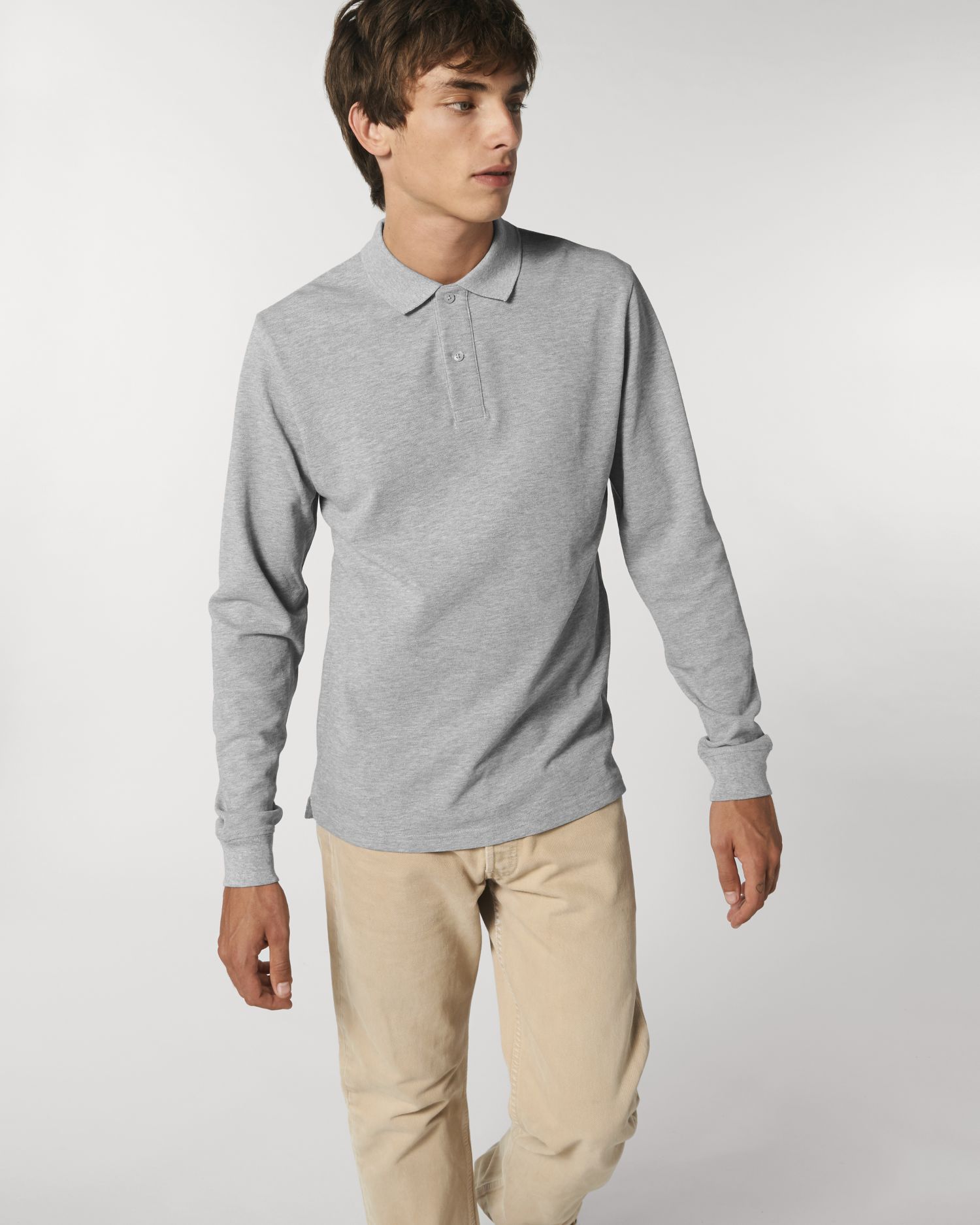 Hombre joven con polo gris de manga larga y pantalones beige sobre fondo neutro