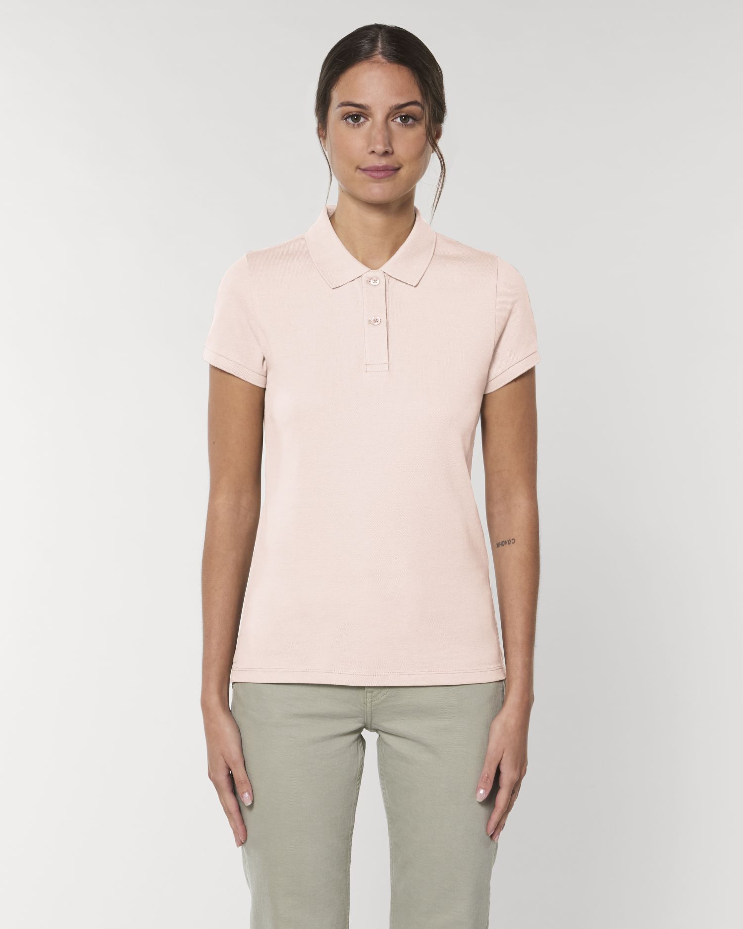 mujer con polo rosa palo y pantalones verdes sobre fondo neutro