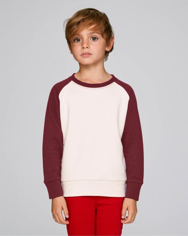 Niño con sudadera de manga raglán crema y granate y pantalones rojos sobre fondo gris claro.
