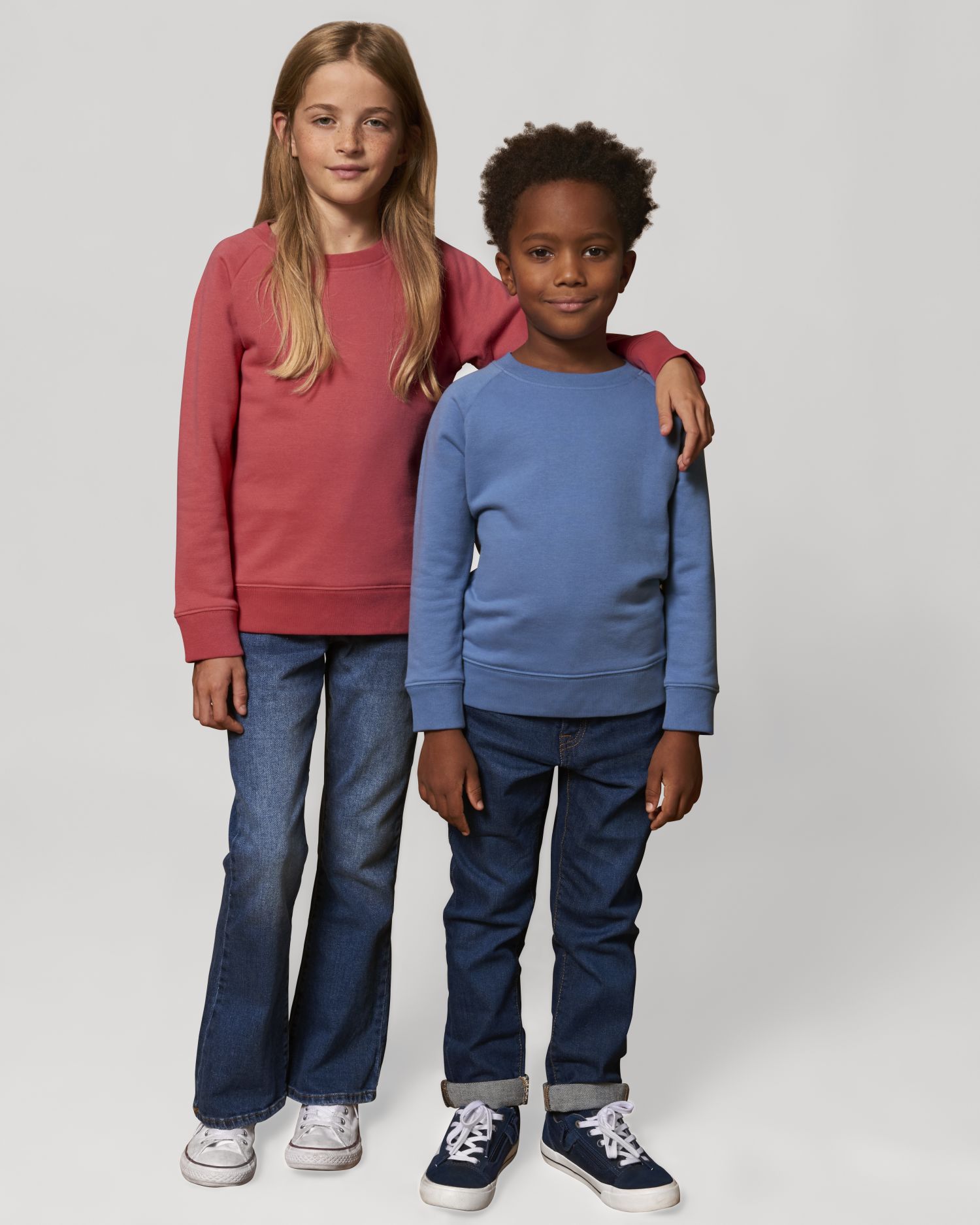 niña y niño de pie con sudaderas lisas y vaqueros en fondo neutro