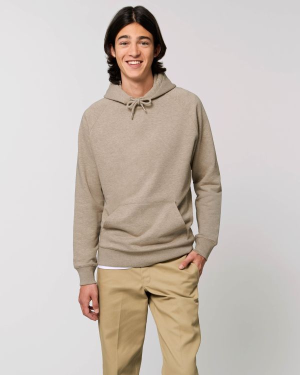 Joven con sudadera con capucha beige y pantalones caqui sonriendo sobre fondo neutro