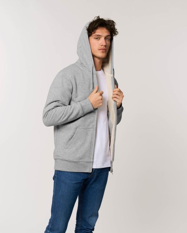 Joven con sudadera gris forrada de borreguillo, camiseta blanca y vaqueros sobre fondo neutro