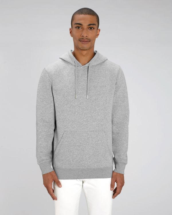 Hombre joven con sudadera gris de capucha y pantalones blancos sobre fondo neutro.