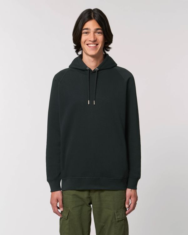 joven sonriente con sudadera negra de capucha y pantalones verdes sobre fondo neutro