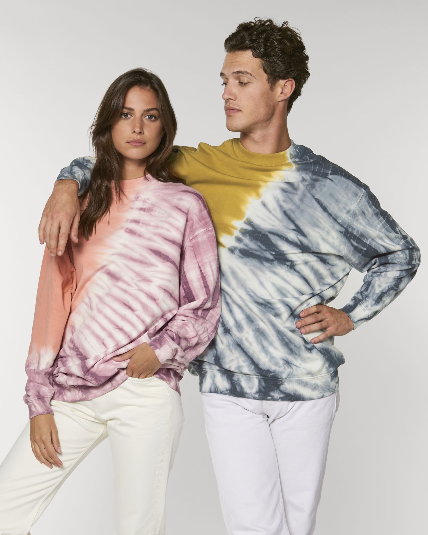 Pareja posando con sudaderas tie-dye en tonos rosa y gris sobre fondo blanco
