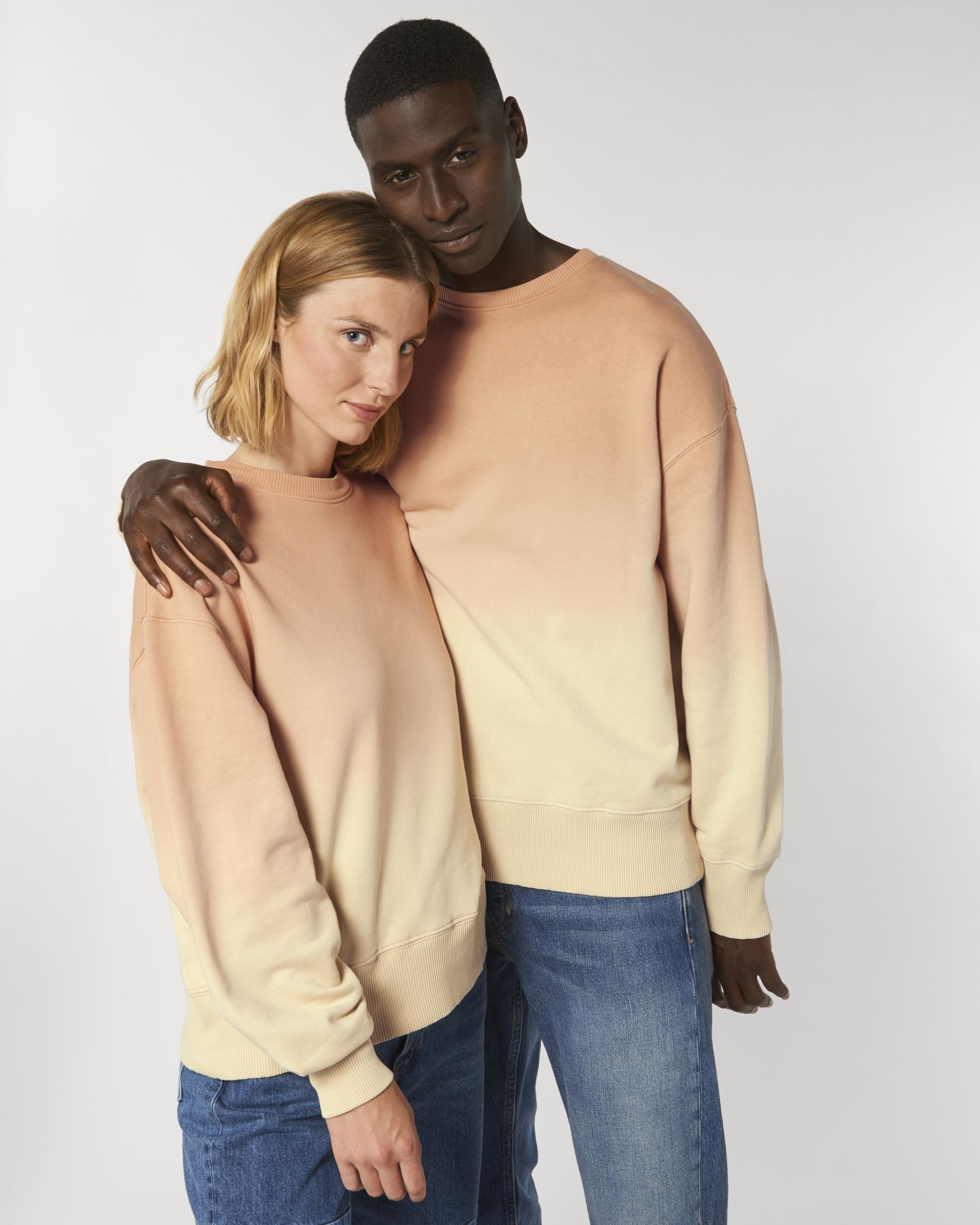 Pareja con sudaderas degradadas en tonos salmón y crema abrazados de pie.