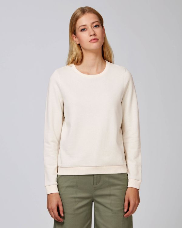 mujer joven de pie con sudadera blanca y pantalones verdes sobre fondo neutro