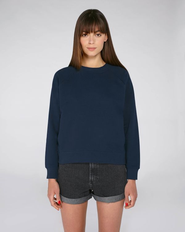 Mujer joven de pie con sudadera azul marino y shorts vaqueros oscuros sobre fondo blanco