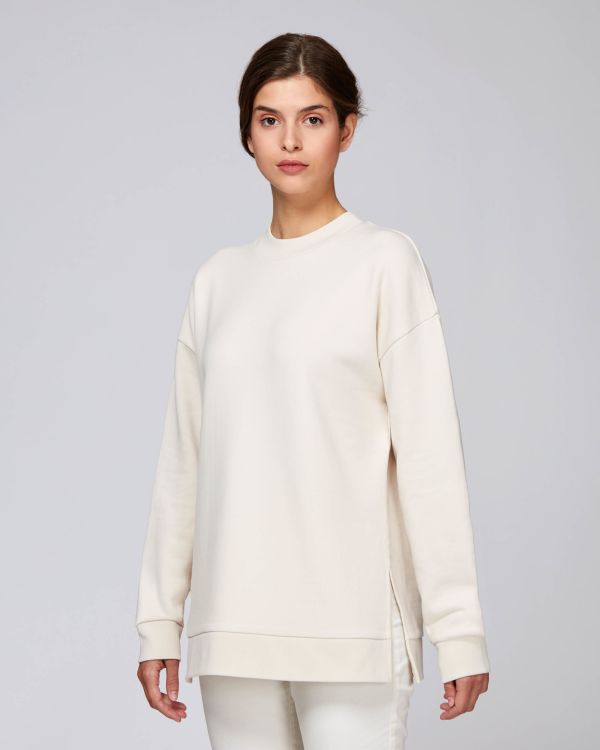 Mujer con sudadera oversize color crema y pantalón blanco sobre fondo gris claro