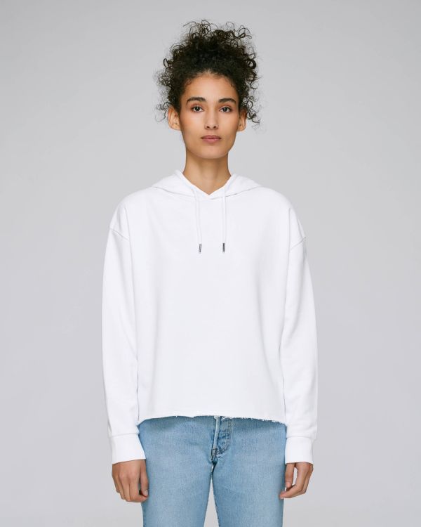 Mujer joven de pie con sudadera blanca con capucha y vaqueros azules sobre fondo gris claro