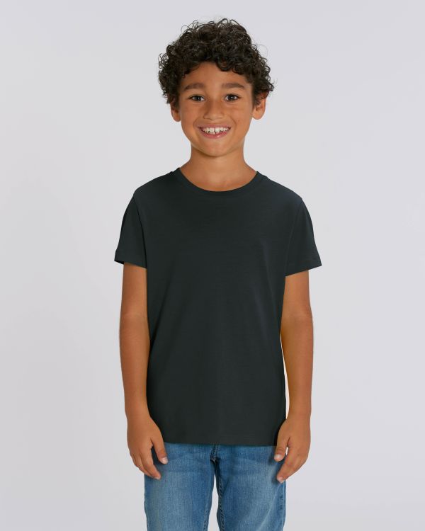niño sonriente con camiseta negra de manga corta y vaqueros sobre fondo blanco