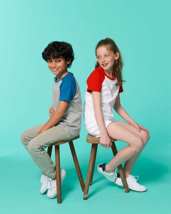 niño y niña sentados de espaldas en taburetes sobre fondo turquesa