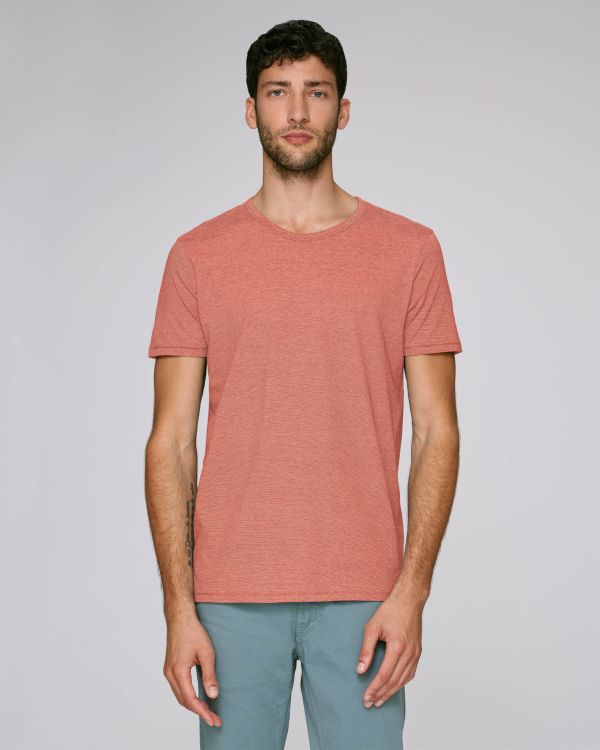 hombre joven de pie con camiseta coral de manga corta y pantalones verde agua sobre fondo neutro