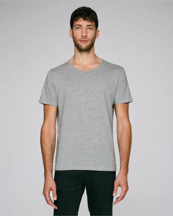 hombre joven de pie con camiseta gris de manga corta y vaqueros negros sobre fondo neutro