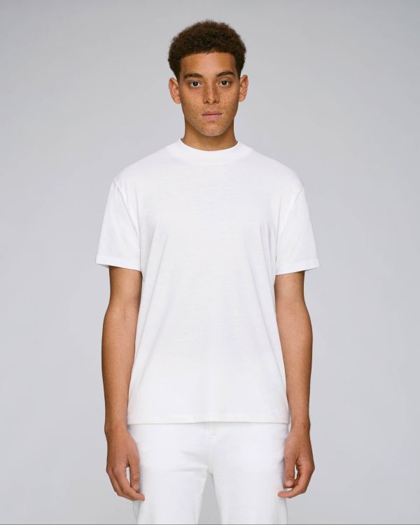 Hombre joven con pelo rizado corto y camiseta blanca de manga corta sobre fondo gris claro.