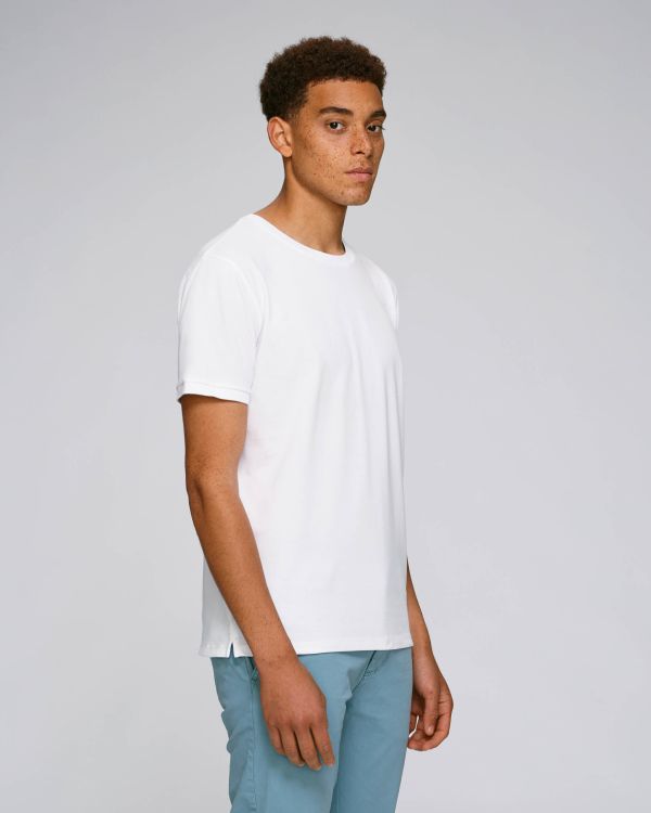 hombre joven con camiseta blanca de manga corta y pantalones azul claro posando de perfil sobre fondo gris claro