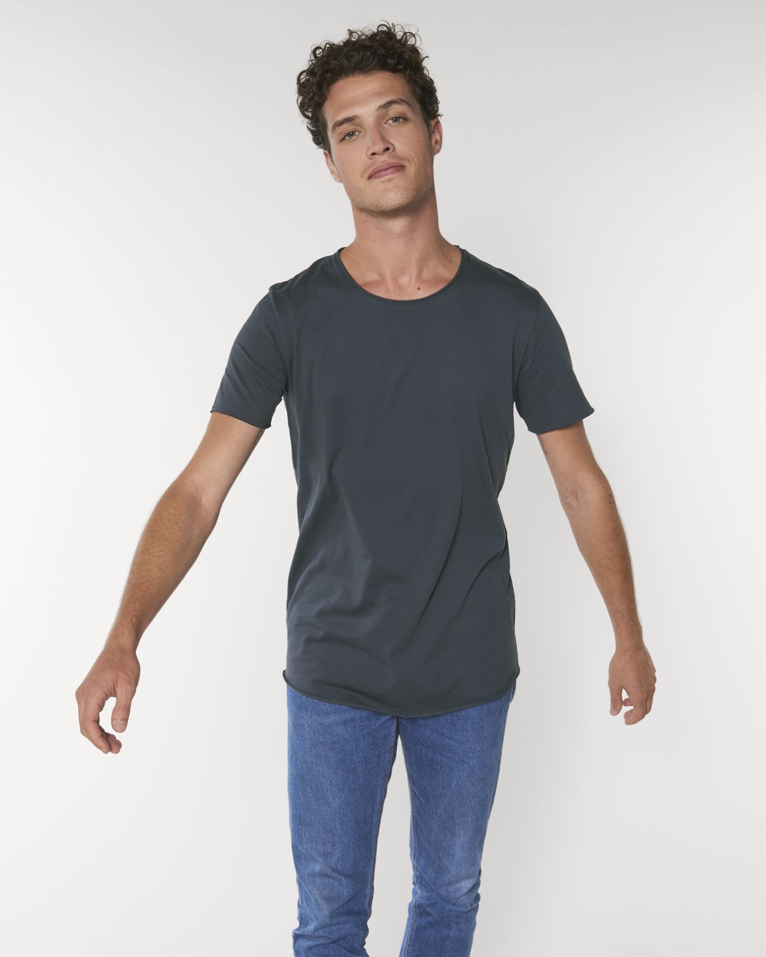 hombre joven con camiseta gris oscuro y vaqueros azules posando sobre fondo blanco