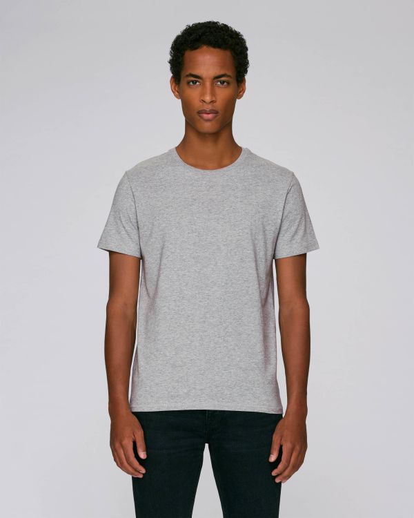 hombre joven con camiseta gris y vaqueros oscuros sobre fondo neutro