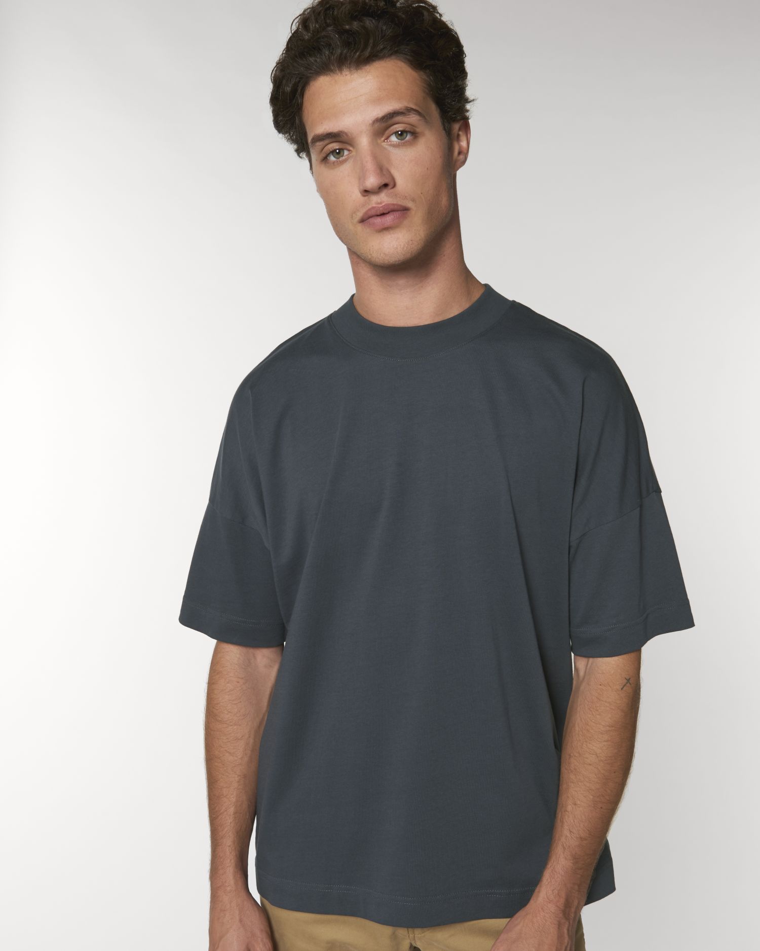 Hombre joven con camiseta holgada gris oscuro y pantalones beige sobre fondo blanco