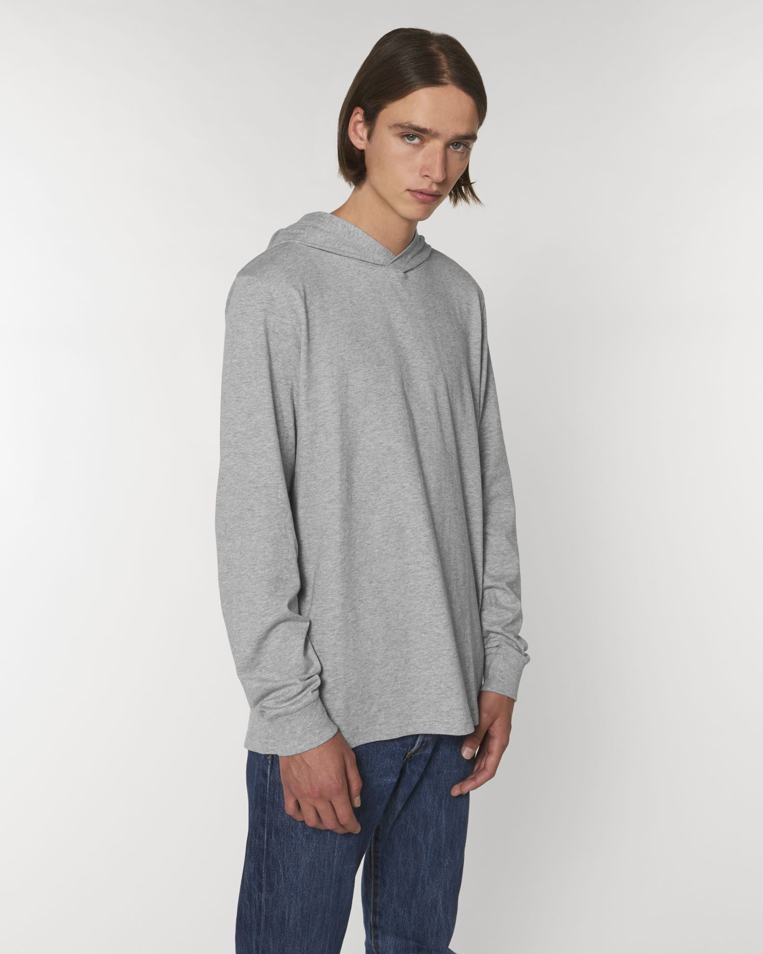 Hombre joven con sudadera gris de manga larga y capucha sobre fondo blanco.