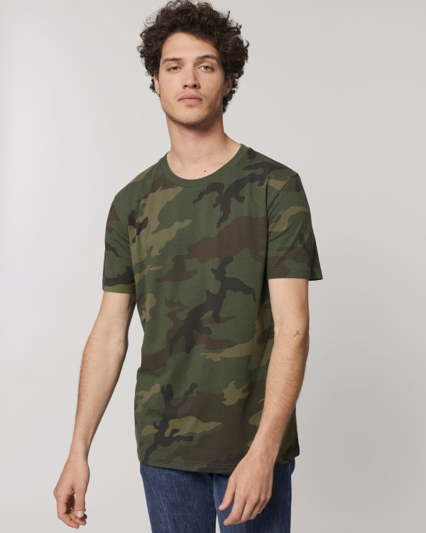 Hombre joven con camiseta de camuflaje verde y vaqueros sobre fondo neutro