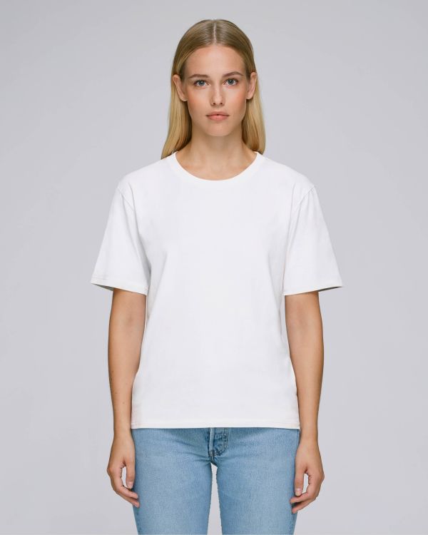 Mujer de pie vistiendo camiseta blanca lisa y vaqueros azules sobre fondo neutro.