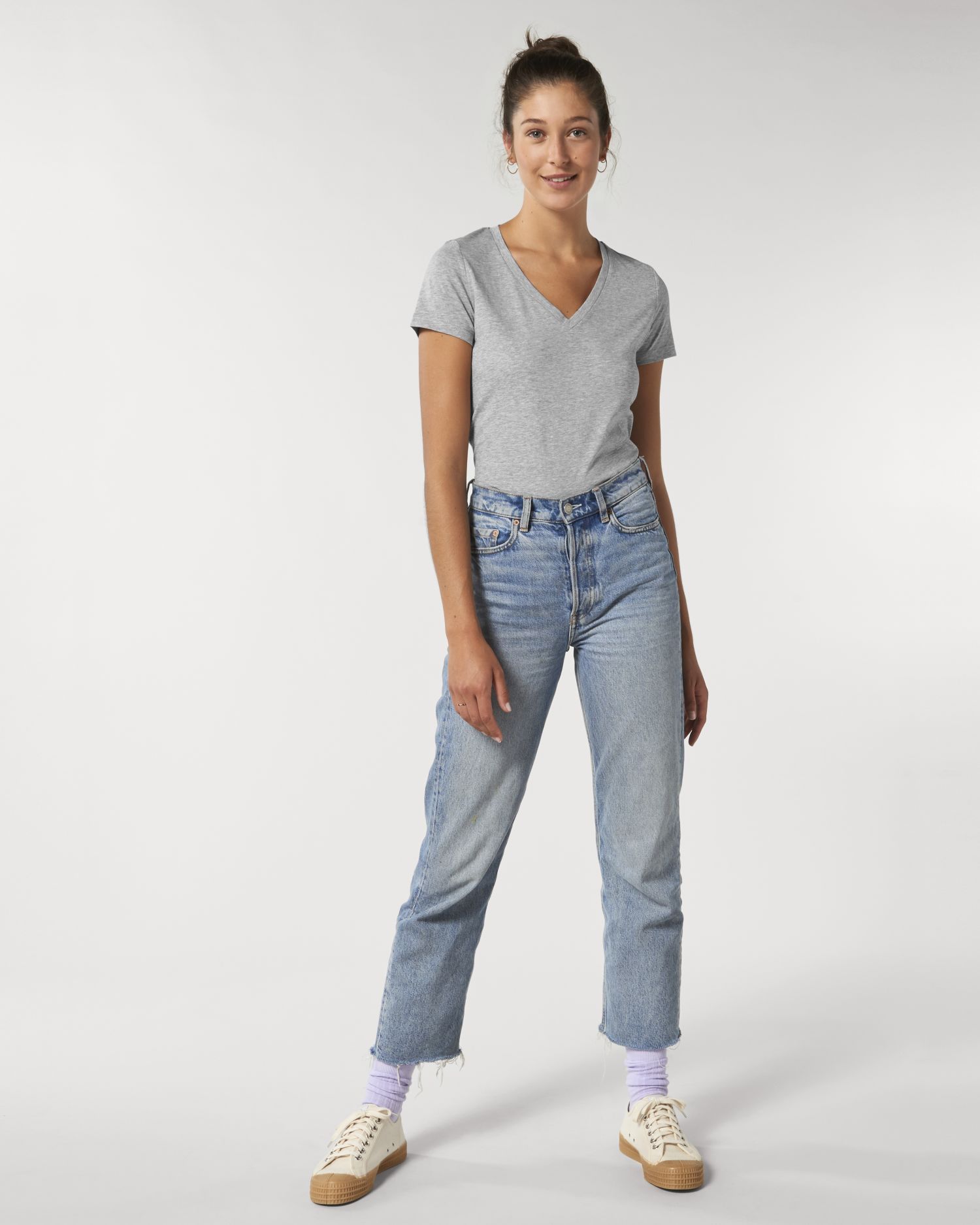 Mujer con camiseta gris de escote en pico y vaqueros azules posando sobre fondo blanco