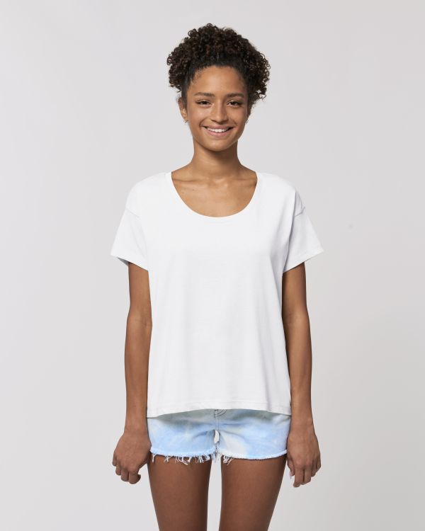 Mujer sonriente con camiseta blanca y shorts vaqueros claros sobre fondo neutro.