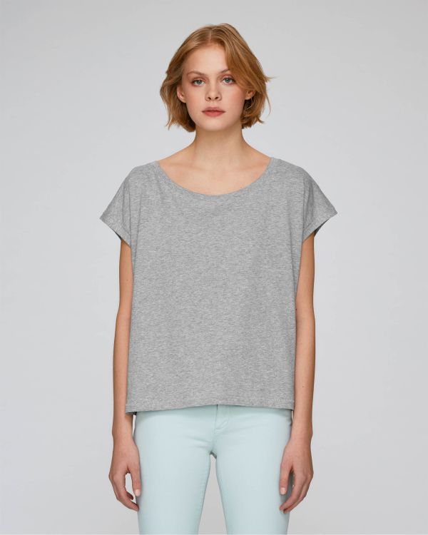 mujer de pie con camiseta gris de manga corta y pantalones azul claro sobre fondo neutro