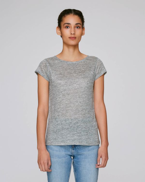 mujer joven de pie con camiseta gris básica y vaqueros claros sobre fondo neutro