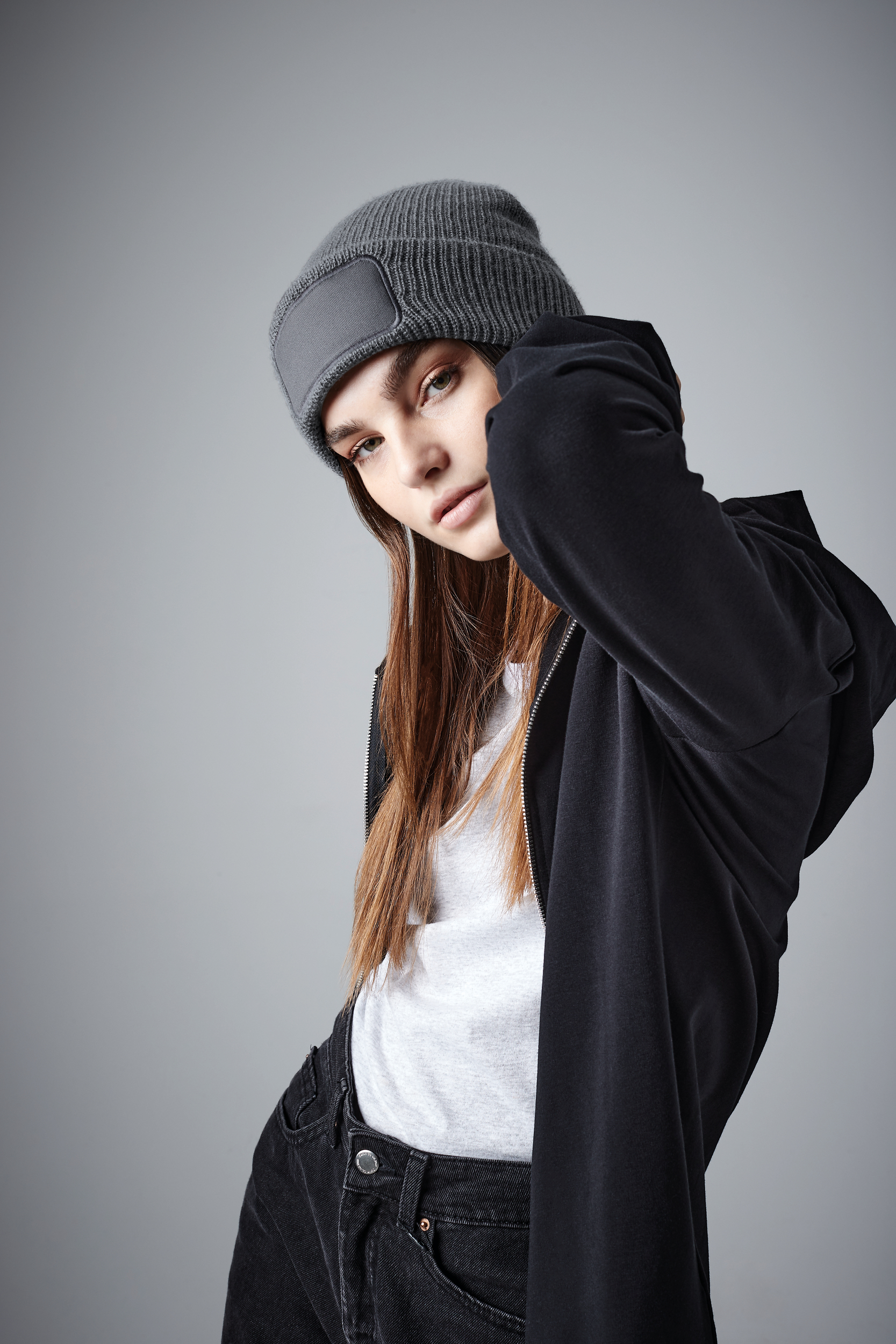 mujer joven con gorro de punto gris y sudadera negra posando sobre fondo neutro