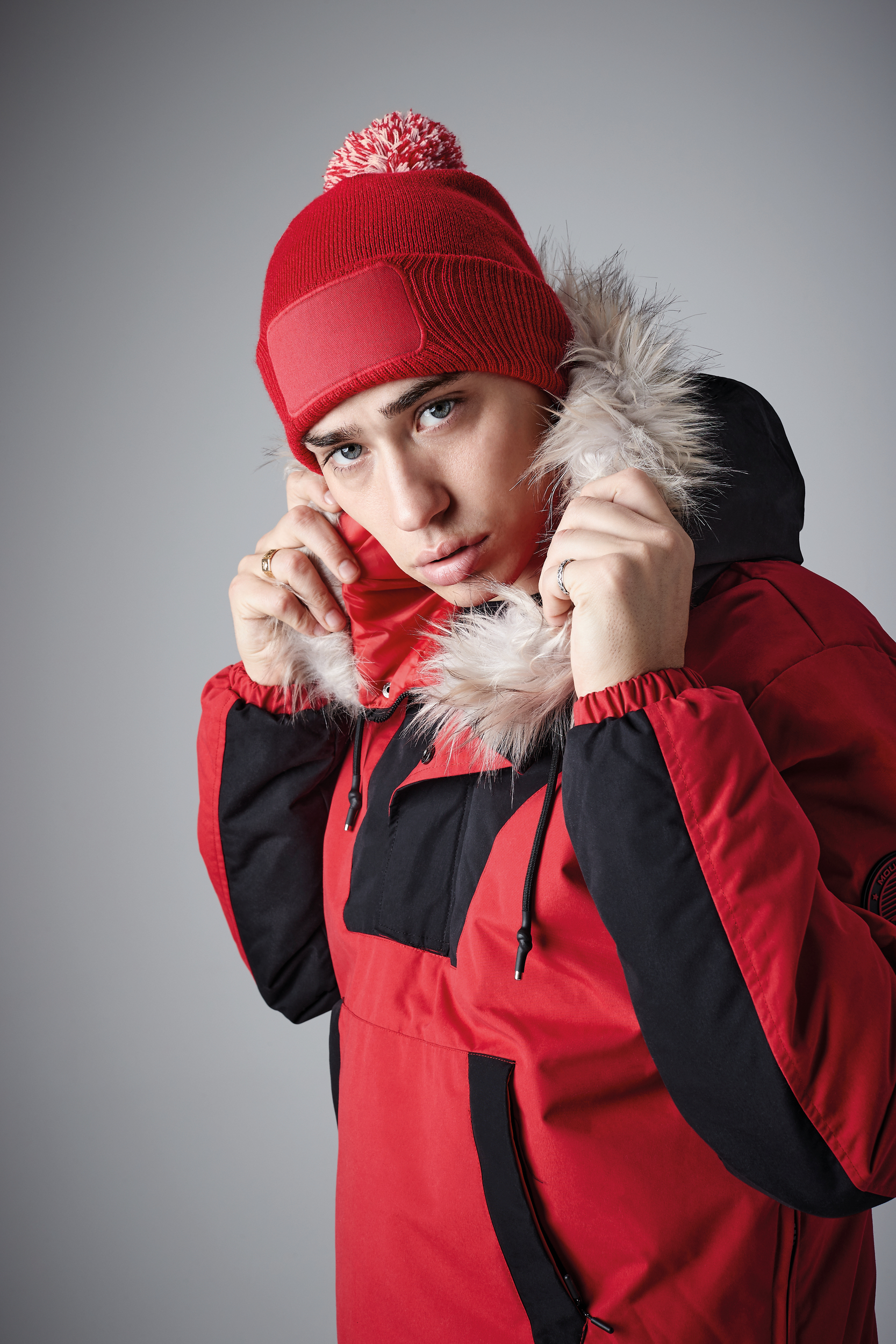 Joven ajustándose la capucha de un abrigo rojo con forro de pelo sintético y gorro de punto rojo