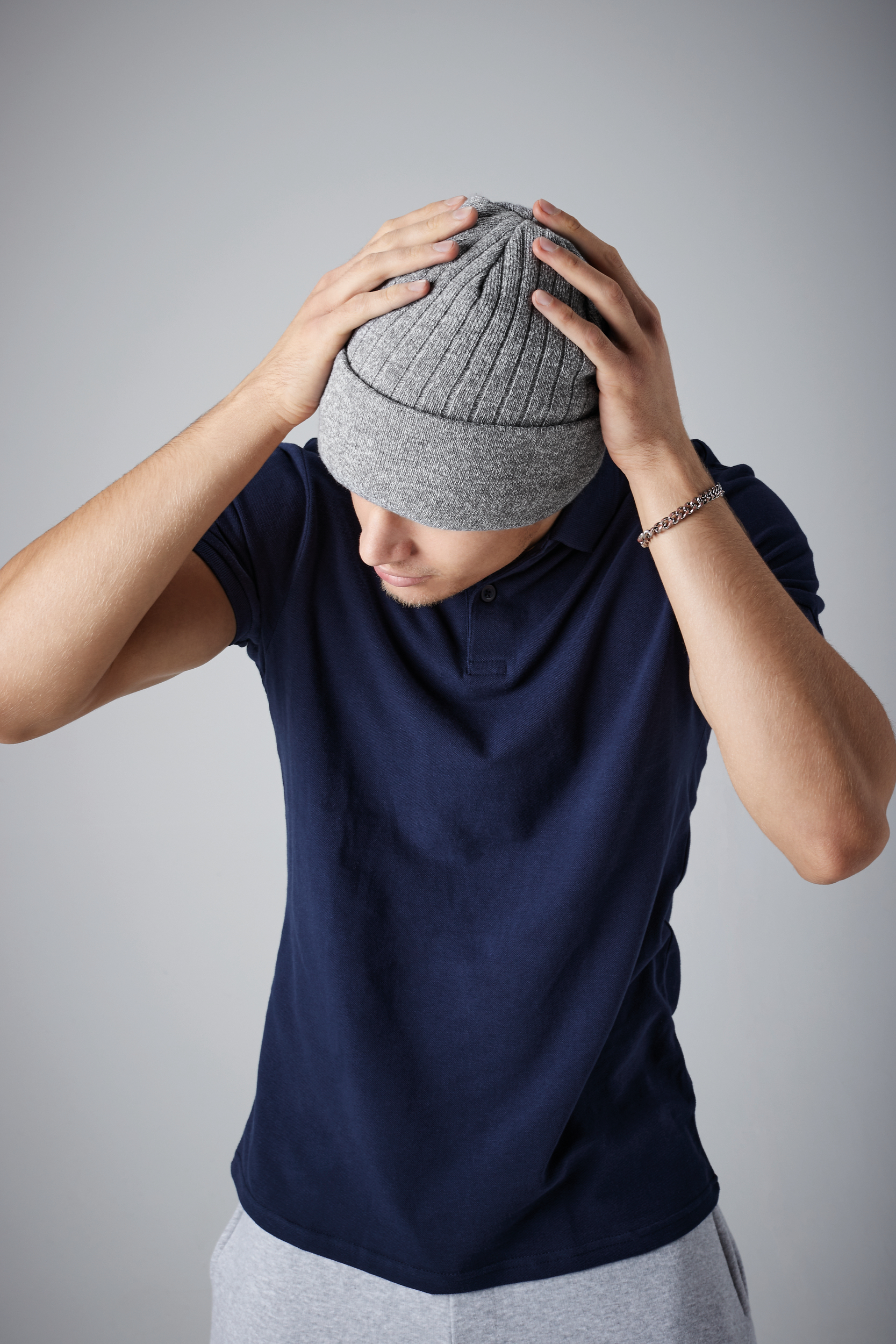 hombre joven con gorro de punto gris y camiseta polo azul ajustándose el gorro sobre fondo neutro