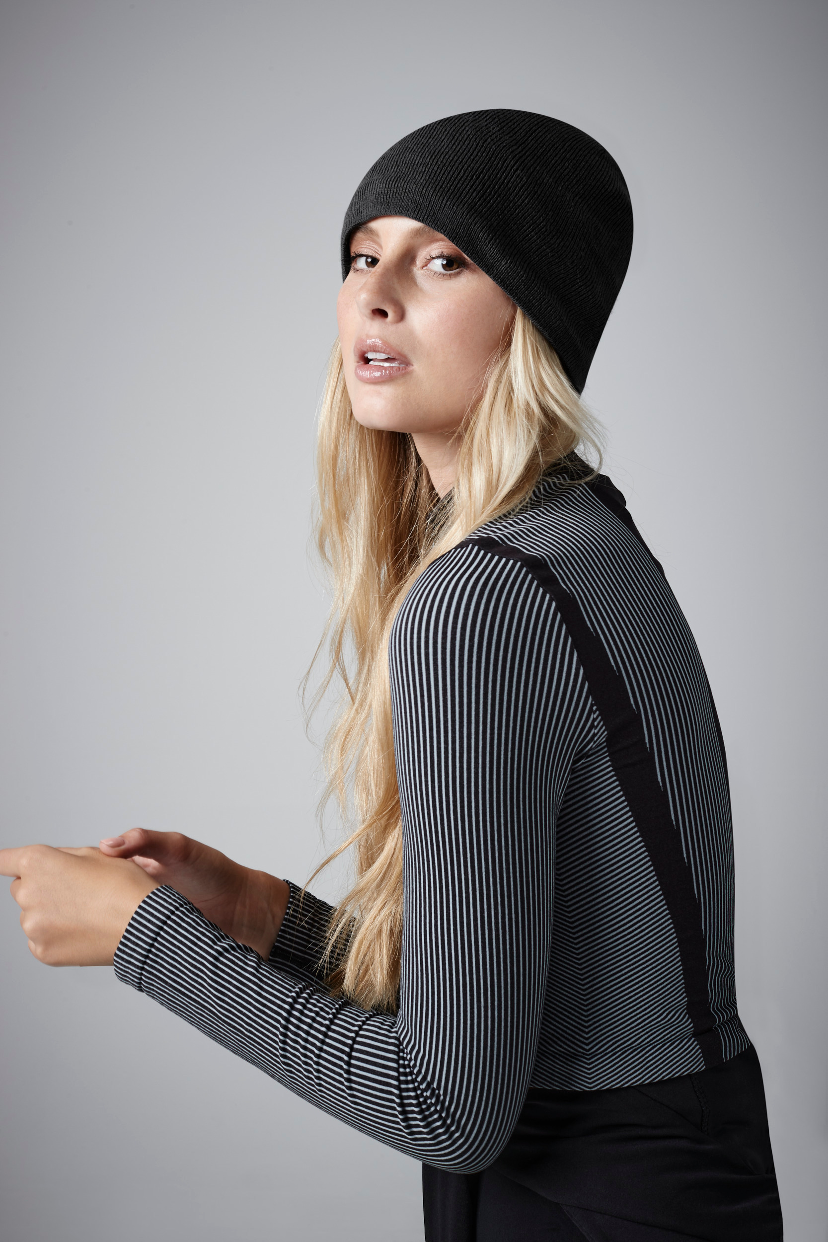 Mujer de perfil con gorro negro y top de rayas sobre fondo neutro