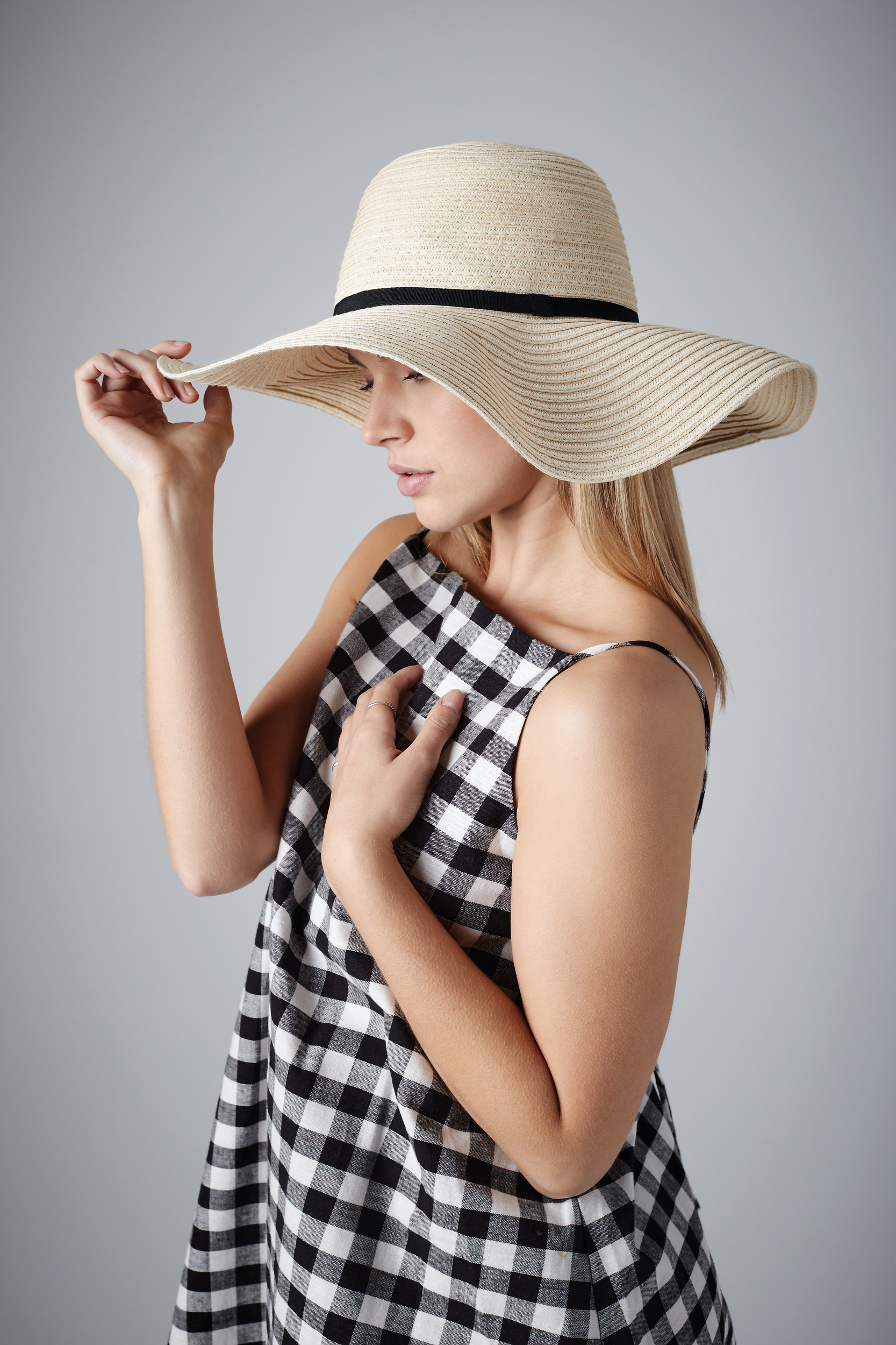 Mujer con vestido de cuadros blanco y negro y sombrero de paja de ala ancha posando sobre fondo gris
