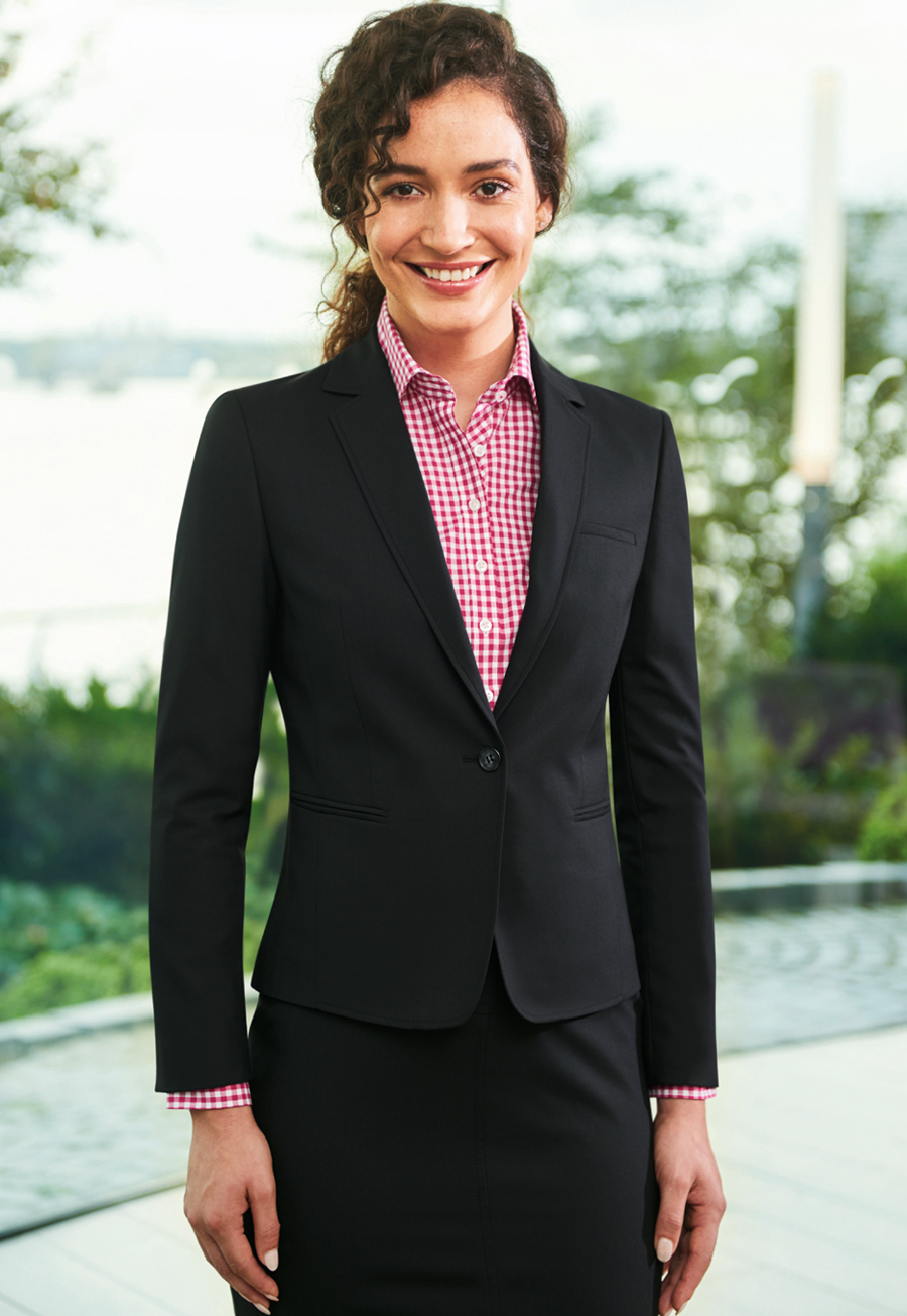 Mujer de negocios sonriente con chaqueta negra y camisa de cuadros rosa junto a un paseo acuático.