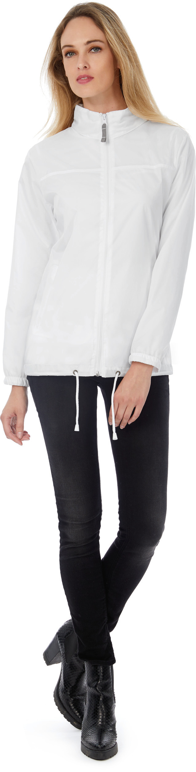 Mujer de pie con chaqueta blanca de cremallera, vaqueros ajustados negros y botines negros de tacón.