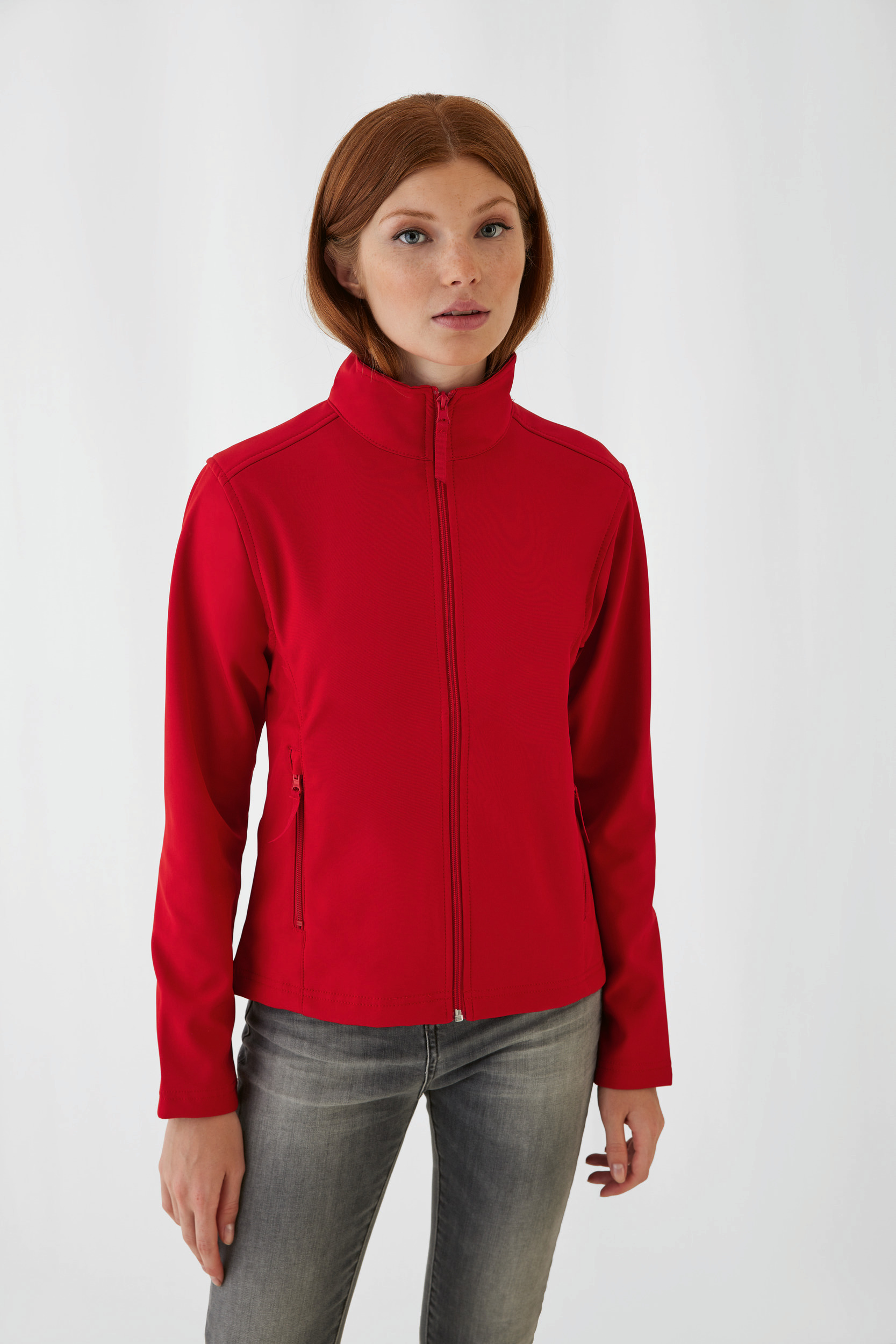 Mujer con chaqueta softshell roja de cremallera y vaqueros sobre fondo blanco