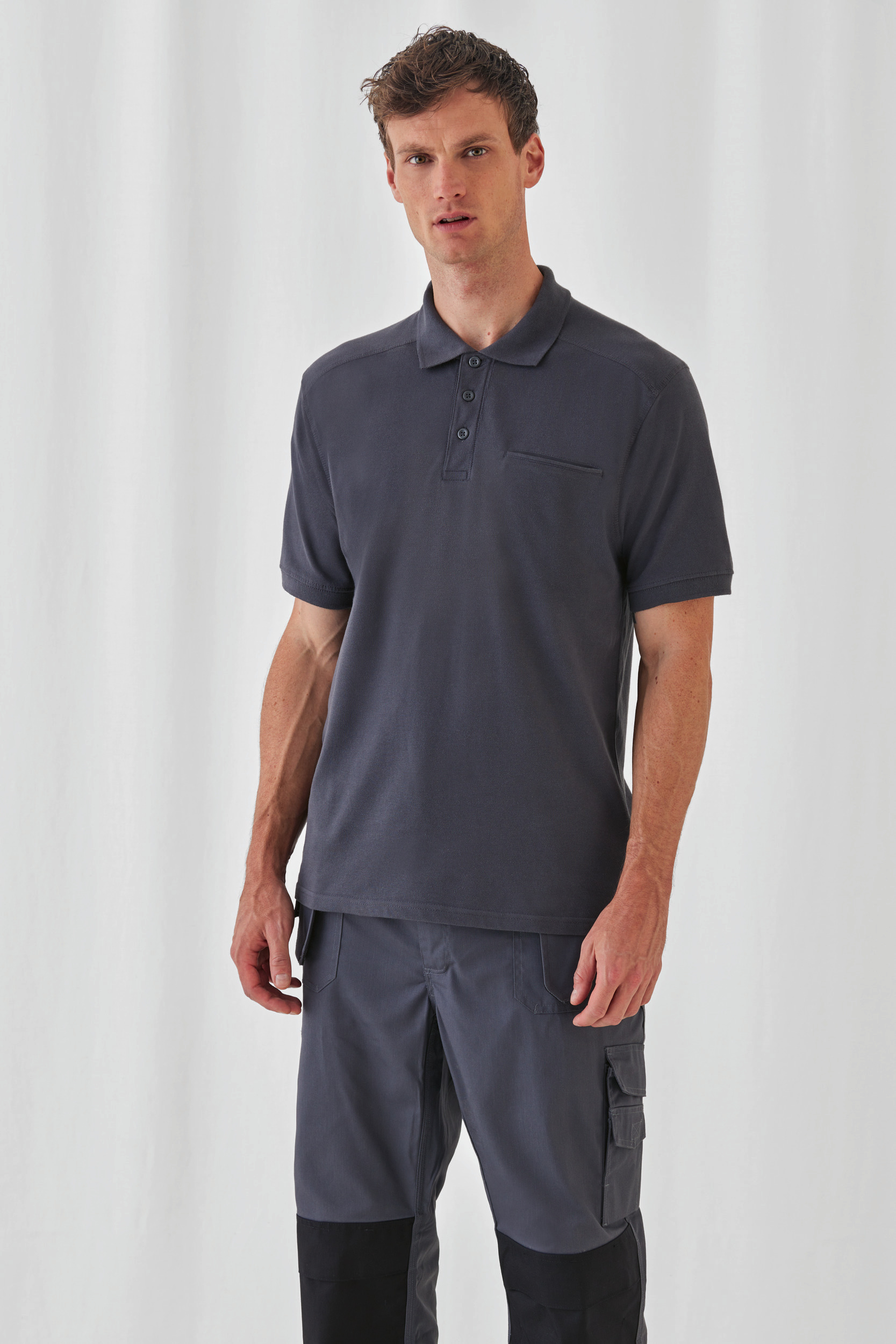 Hombre con polo azul marino de manga corta y pantalones cargo grises sobre fondo neutro