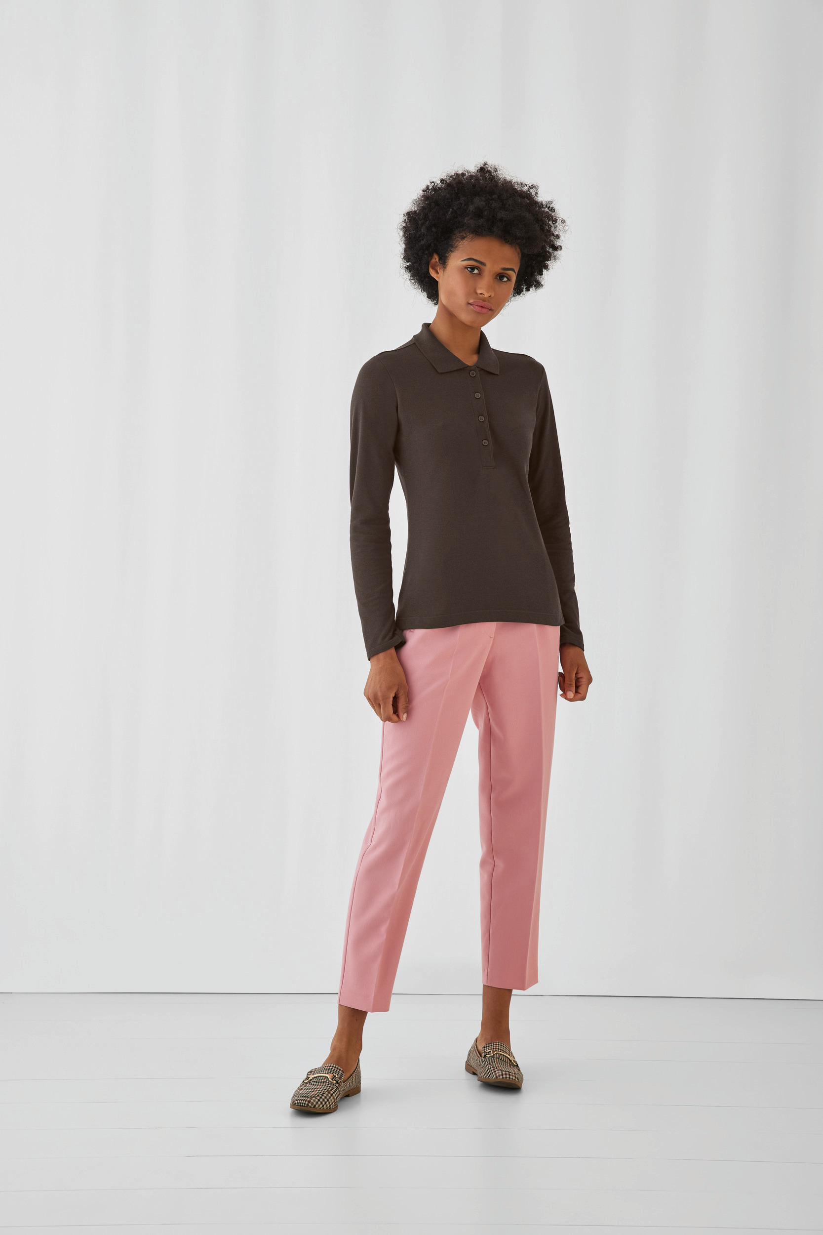 Mujer con polo negro de manga larga y pantalones rosas de corte recto sobre fondo blanco.