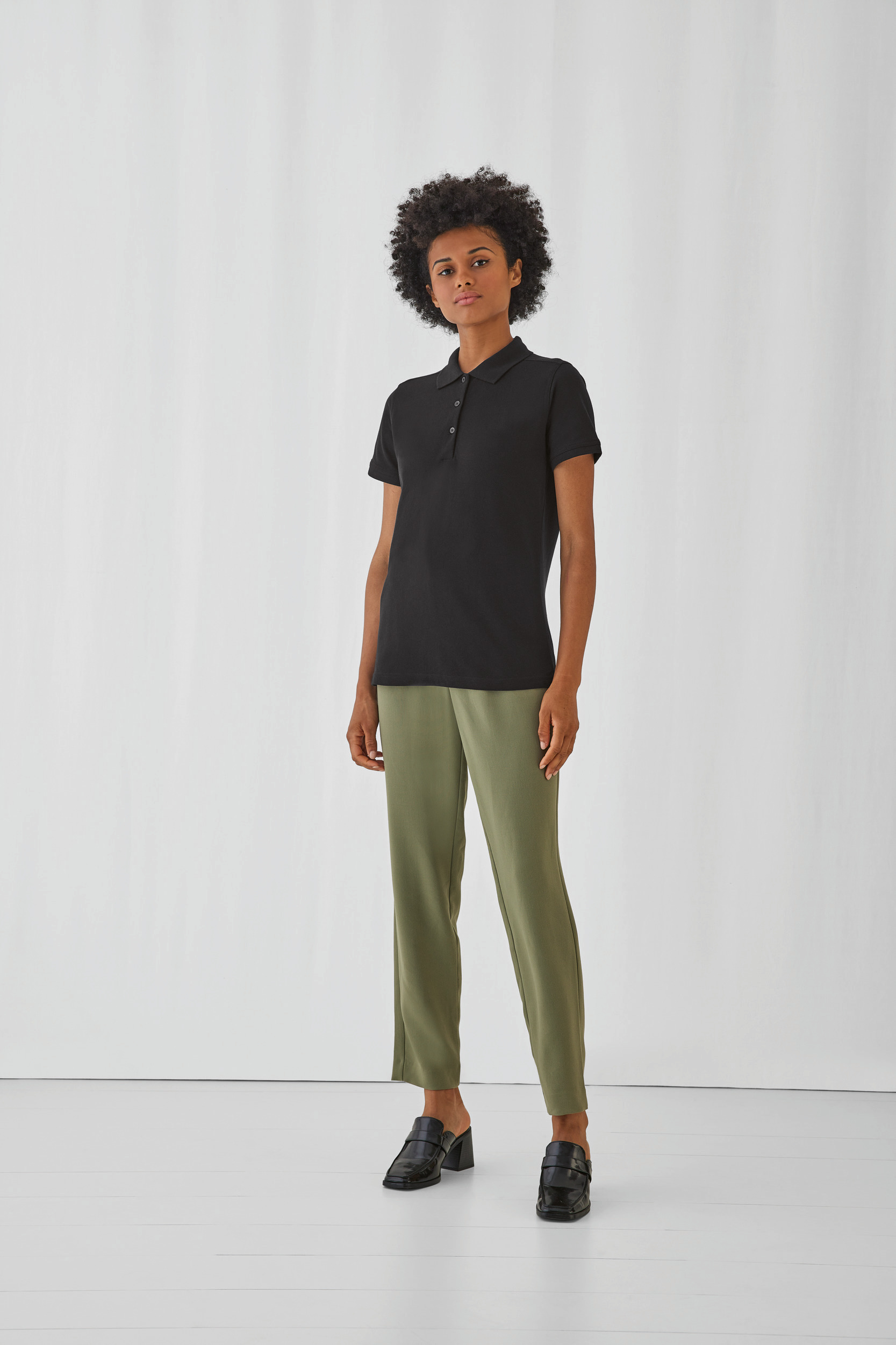 Modelo con polo negro, pantalones verde oliva y mocasines negros sobre fondo blanco