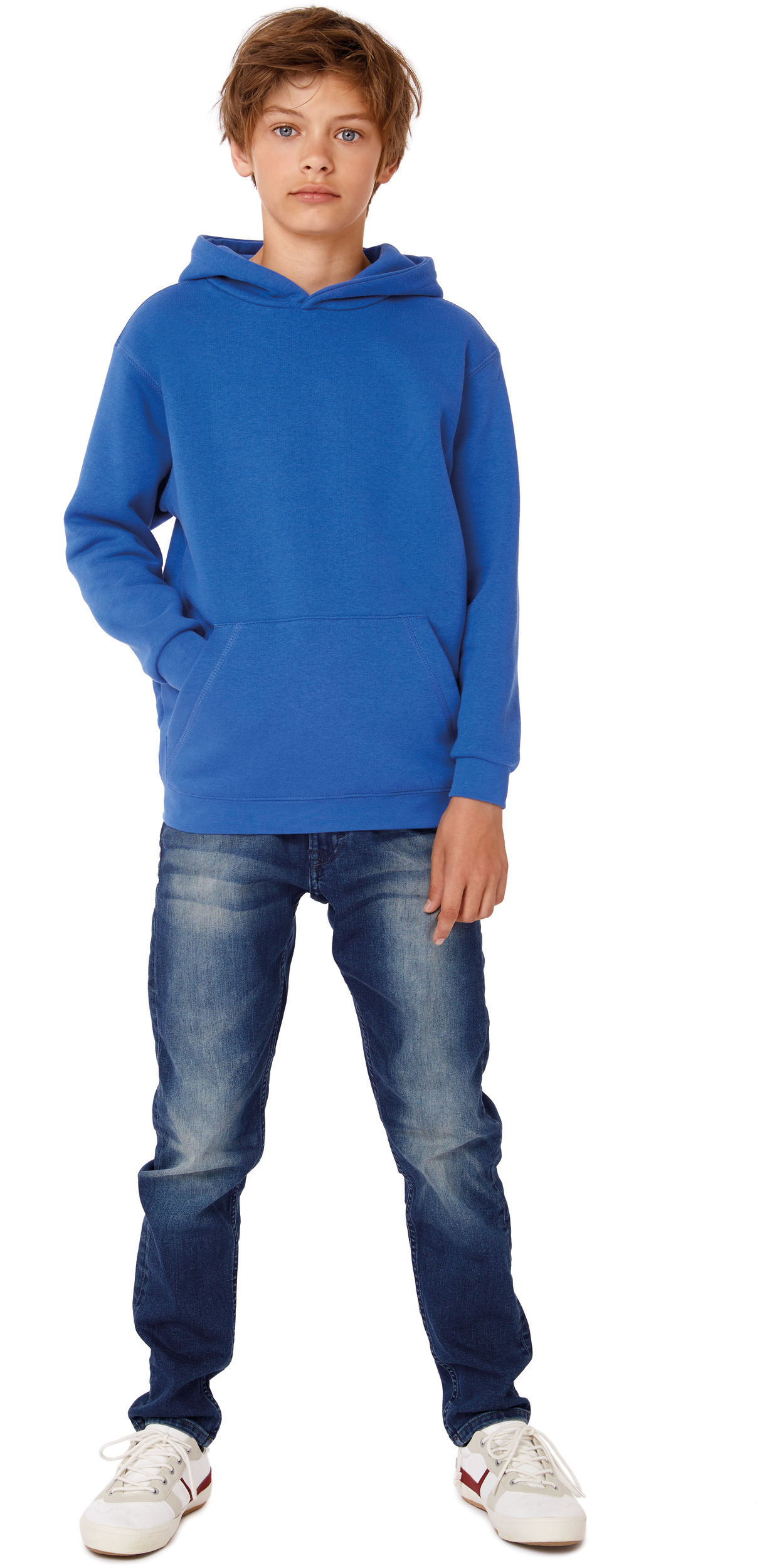 Niño de pie con sudadera azul, vaqueros y zapatillas deportivas sobre fondo blanco.